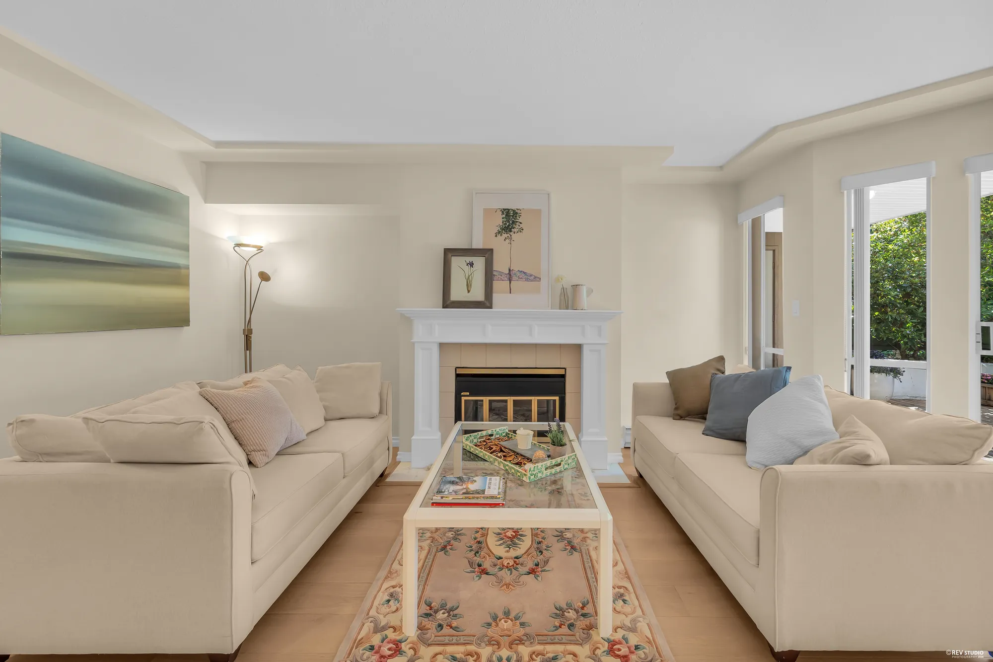 The living room: two sofas, the gas fireplace with a white mantel, and the bay window